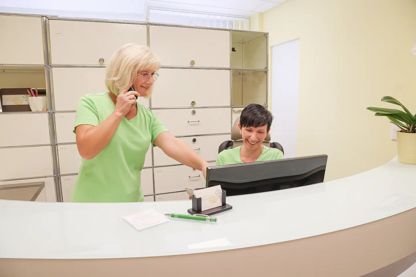 Zwei freundliche Mitarbeiterinnen am Empfang einer Zahnarztpraxis, eine telefoniert.