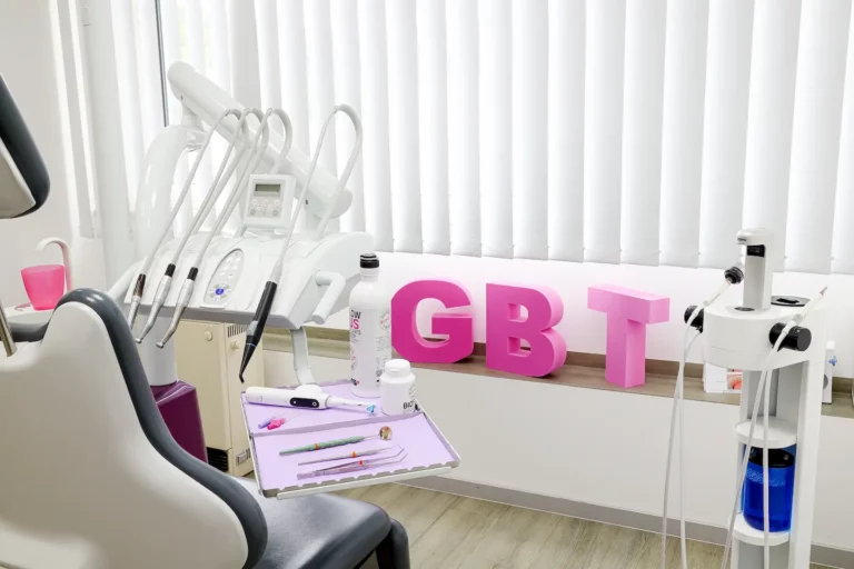 Zahnarztpraxis mit Behandlungsstuhl, Geräten und rosa „GBT“-Buchstaben auf der Fensterbank.
