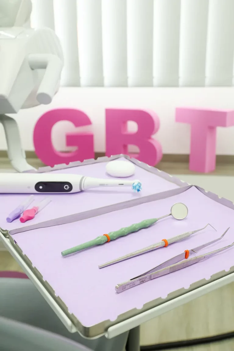 Zahnärztliche Instrumente auf Tablett mit rosa Buchstaben „GBT“ im Hintergrund.