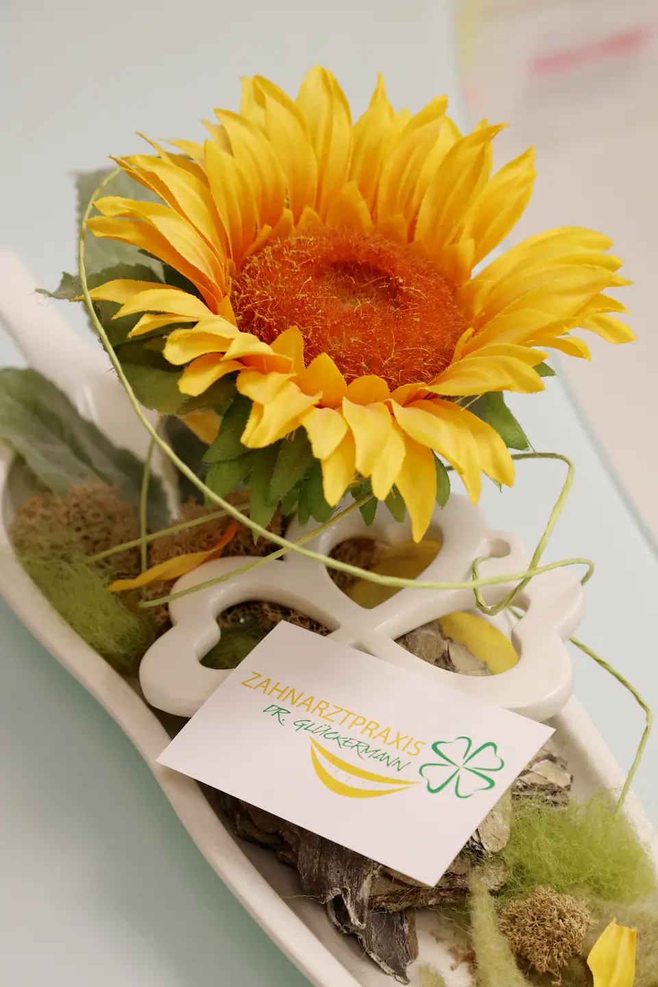 Ein Gesteck mit einer Sonnenblume an dem eine Visitenkarte / Bestellkarte befestigt ist